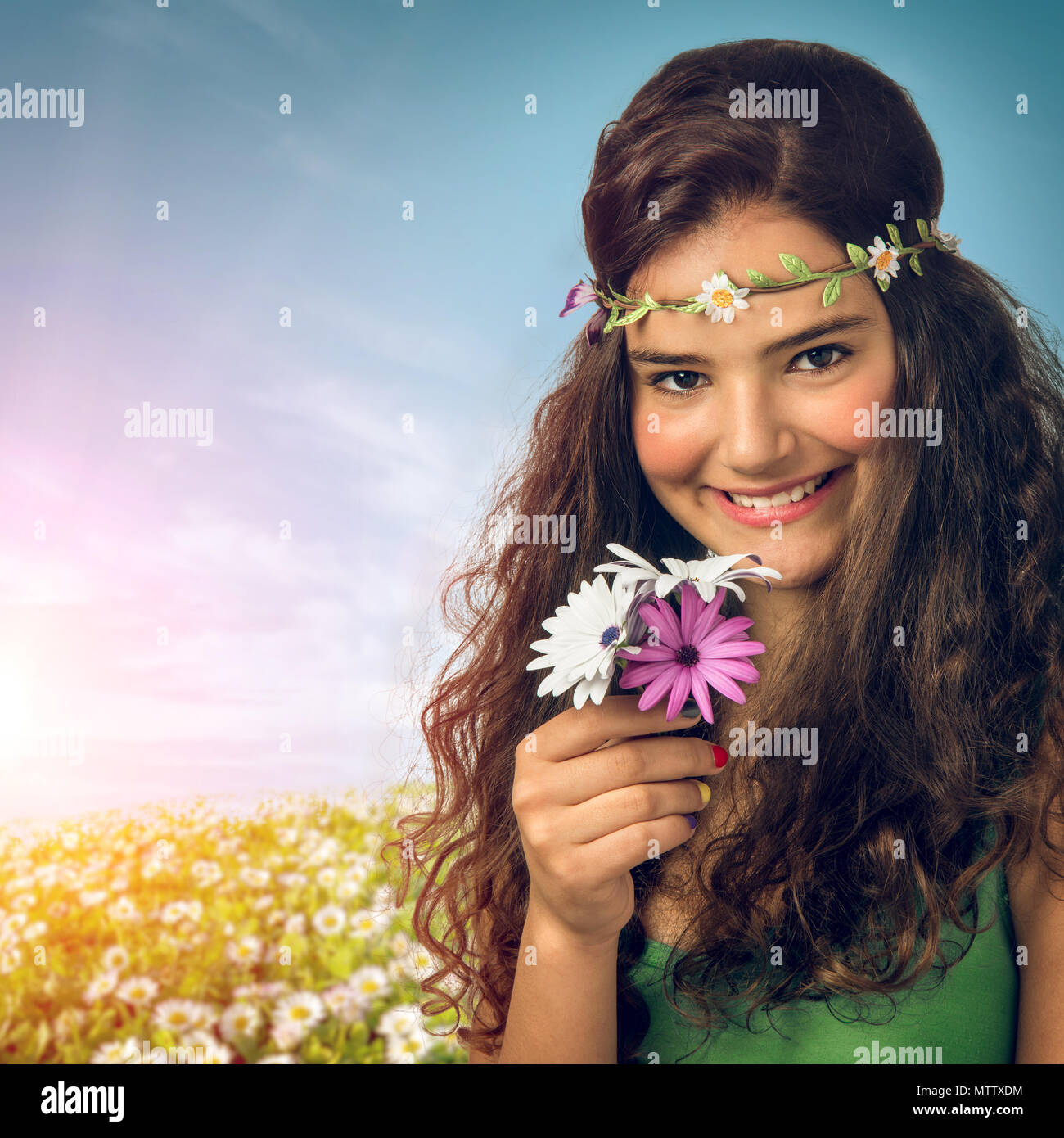 Ragazza giovane e carina con archetto floreali e tenendo i fiori su un campo a molla Foto Stock