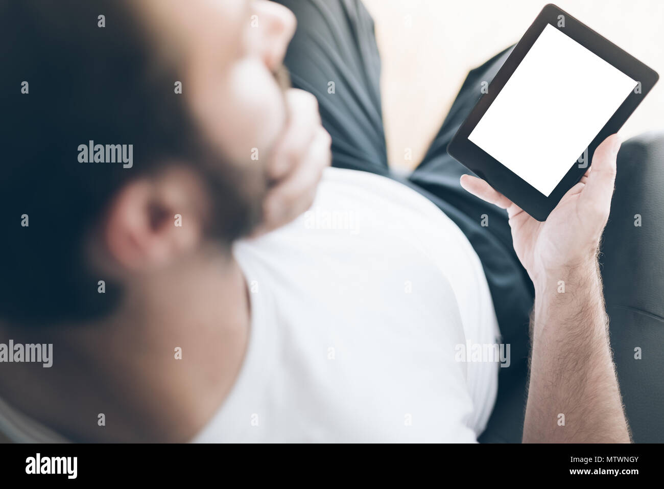 Al di sopra della spalla vista dell uomo seduto sulla poltrona utilizzando l'e-book reader o tablet PC Foto Stock