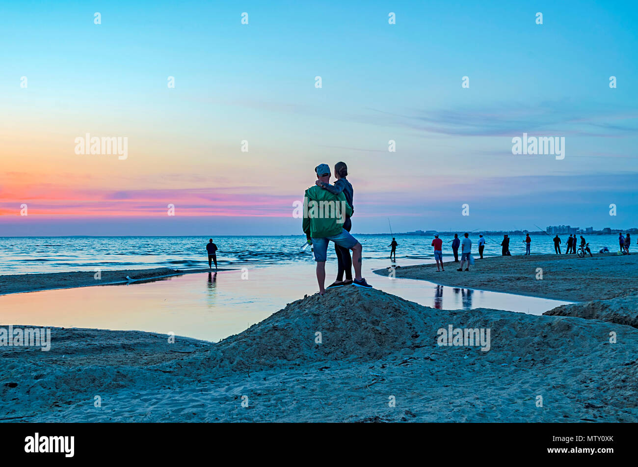 I turisti e i pescatori sono sul mar Nero e ammirare il bellissimo tramonto. Un giovane in amore prende un selfie contro il tramonto. Foto Stock