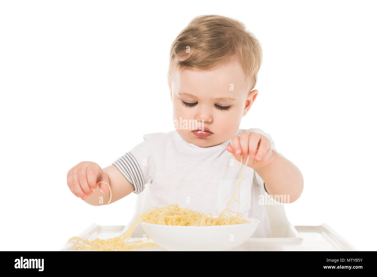 Adorabile bambino mangiare spaghetti con le mani e la seduta nel seggiolone isolati su sfondo bianco Foto Stock