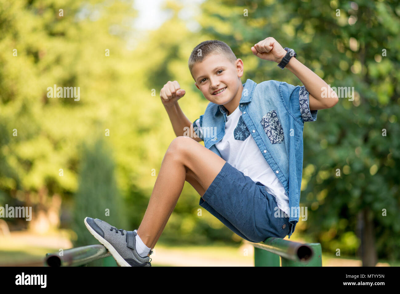 Sorridente ragazzo seduto in posizione di parcheggio la flessione i suoi muscoli Foto Stock