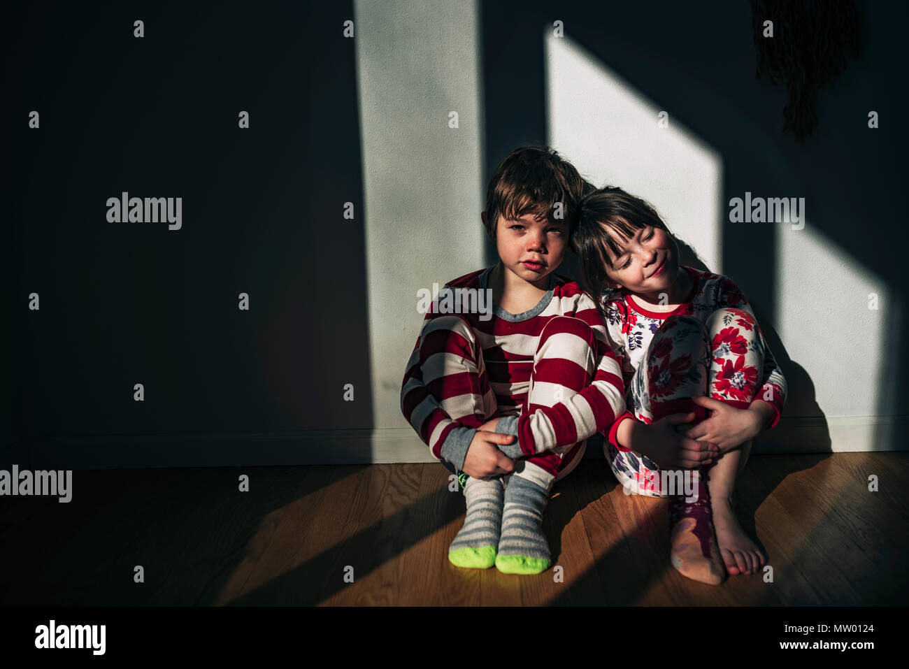 Un ragazzo e una ragazza seduta sul pavimento appoggiato contro una parete Foto Stock