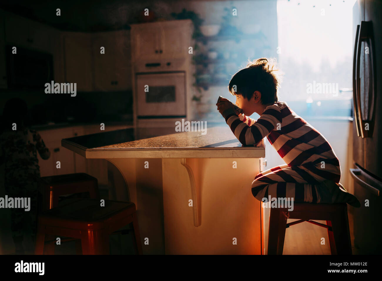 Ragazzo seduto in cucina a mangiare la sua colazione nella luce del mattino Foto Stock