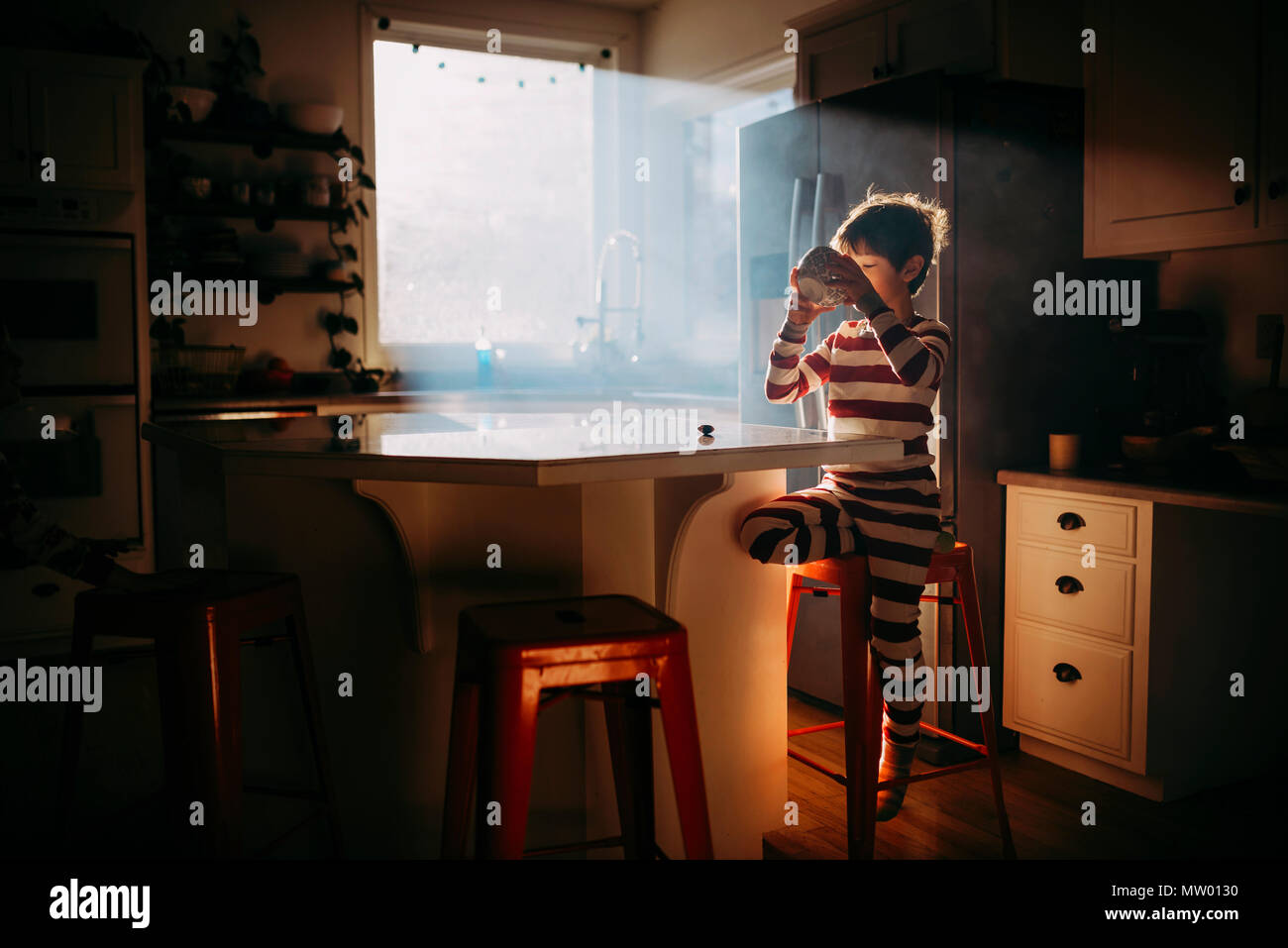 Ragazzo in piedi in cucina a mangiare la sua colazione nella luce del mattino Foto Stock
