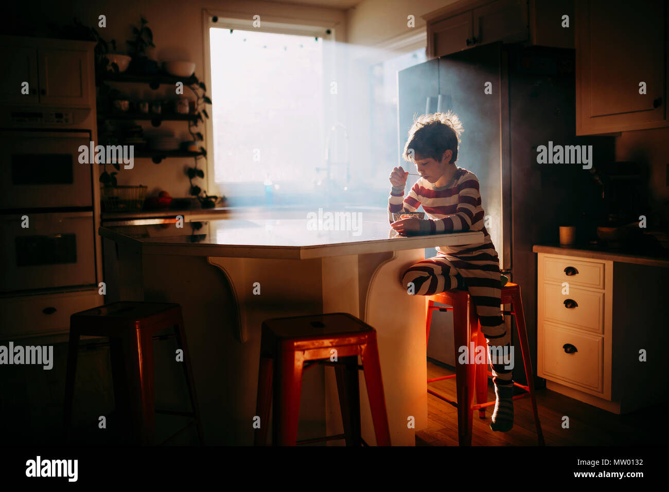 Ragazzo seduto in cucina a mangiare la sua colazione nella luce del mattino Foto Stock