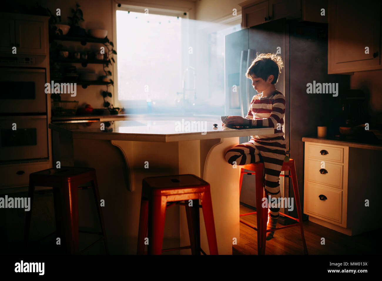 Ragazzo in piedi in cucina a mangiare la sua colazione nella luce del mattino Foto Stock
