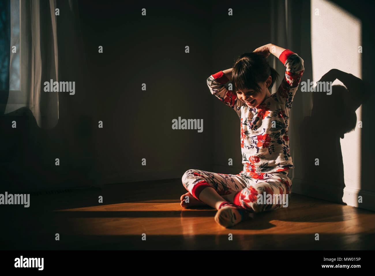 Ragazza seduta sul pavimento in pigiama con le mani nei capelli Foto Stock