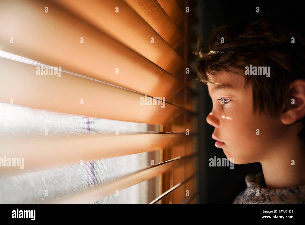Ragazzo accanto a una finestra guardando attraverso le persiane Foto Stock
