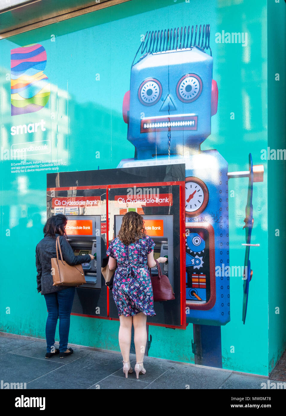 Due giovani donna utilizzando cashpoints al di fuori di una banca Cluydesdale nella zona centrale di Glasgow, Scotland, Regno Unito. Un illustrazione di un robot è sulla parete della banca. Foto Stock