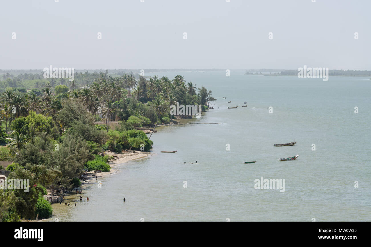 Costa Tropicale linea con stretta spiaggia grigio, palme, vegetazione lussureggiante e legno barche da pesca, Ndiebene, Senegal. Foto Stock