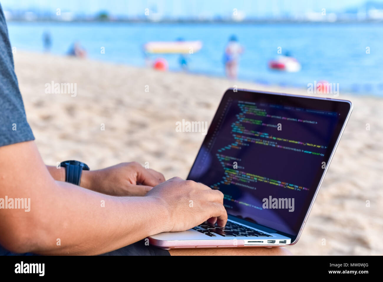 Un programmatore digitando i codici sorgente in spiaggia su una soleggiata giornata estiva. Studiare, lavorare, Tecnologia, freelance lavoro concetto. Foto Stock