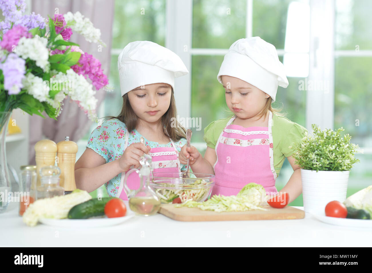 Due adorabili bambine in grembiuli preparare deliziose insalate Foto Stock