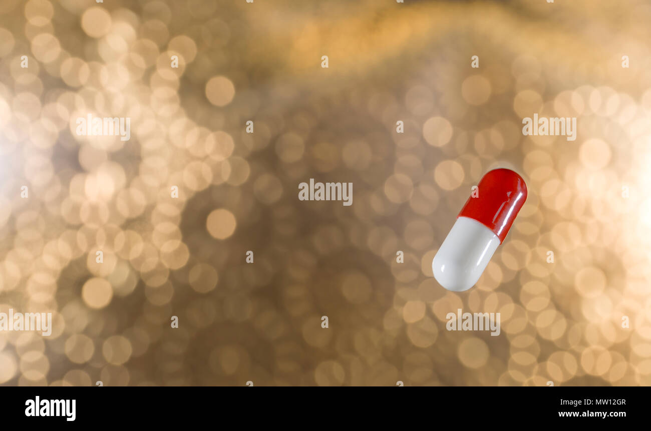 Vista ravvicinata del rosso e del bianco il farmaco antivirale capsula contro fuori fuoco sfondo dorato dandogli un atmosfera di festa Foto Stock