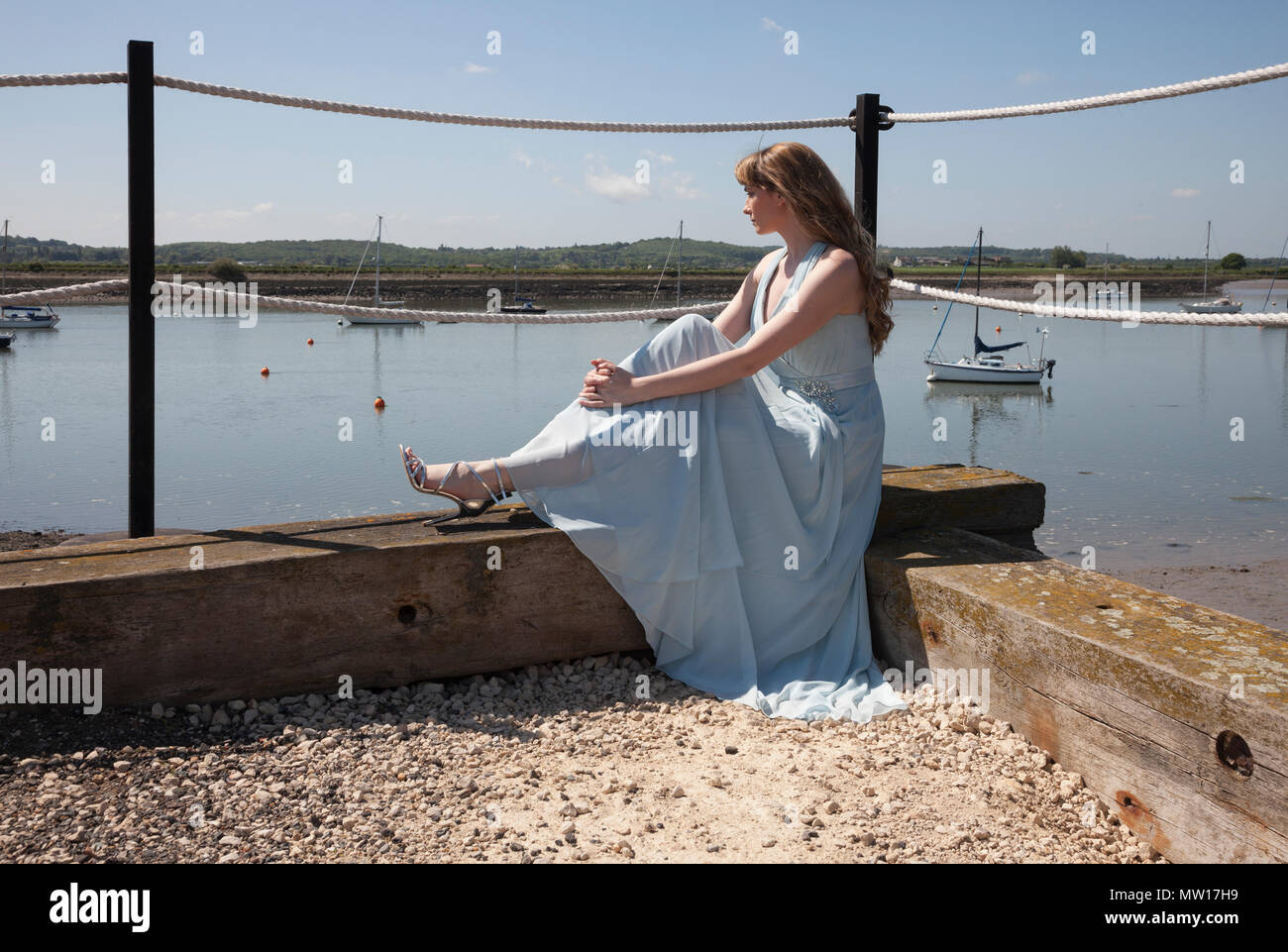Signora seduta sul bordo del molo che si affaccia estuario Foto Stock