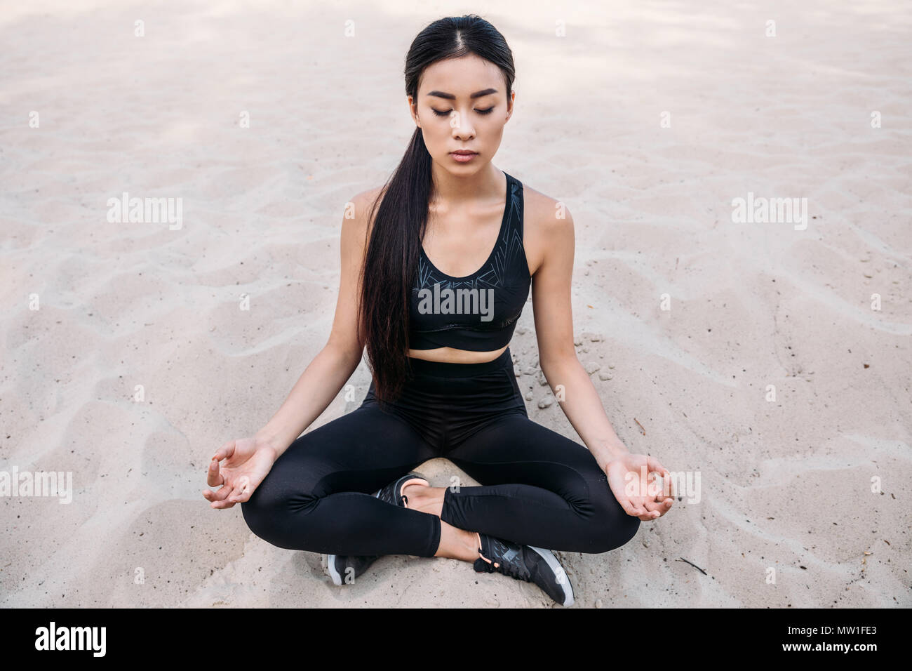 Donna asiatica meditando in lotus yoga pone con gyan mudra sulla sabbia Foto Stock