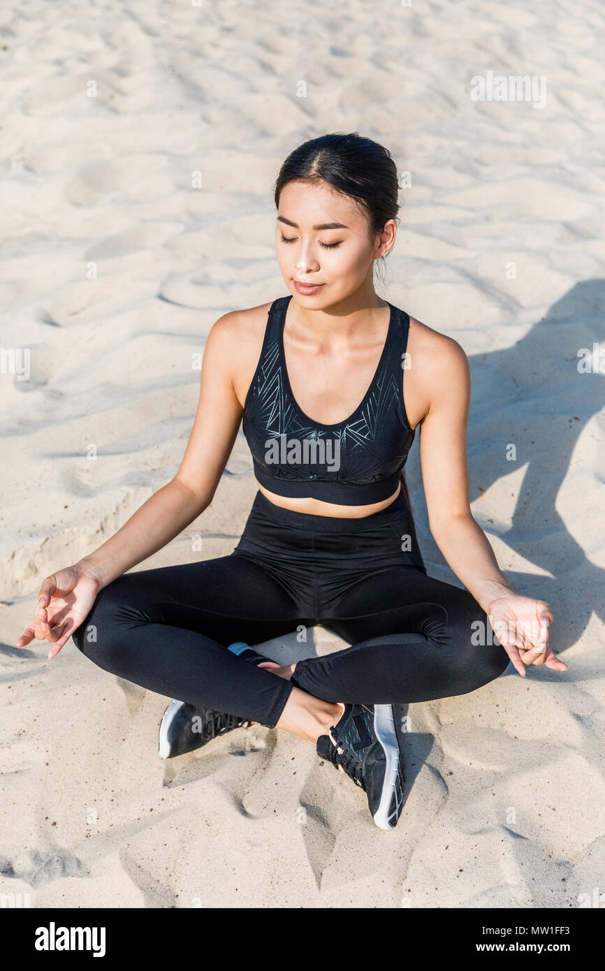 Donna asiatica meditando in lotus yoga pone con gyan mudra sulla sabbia Foto Stock