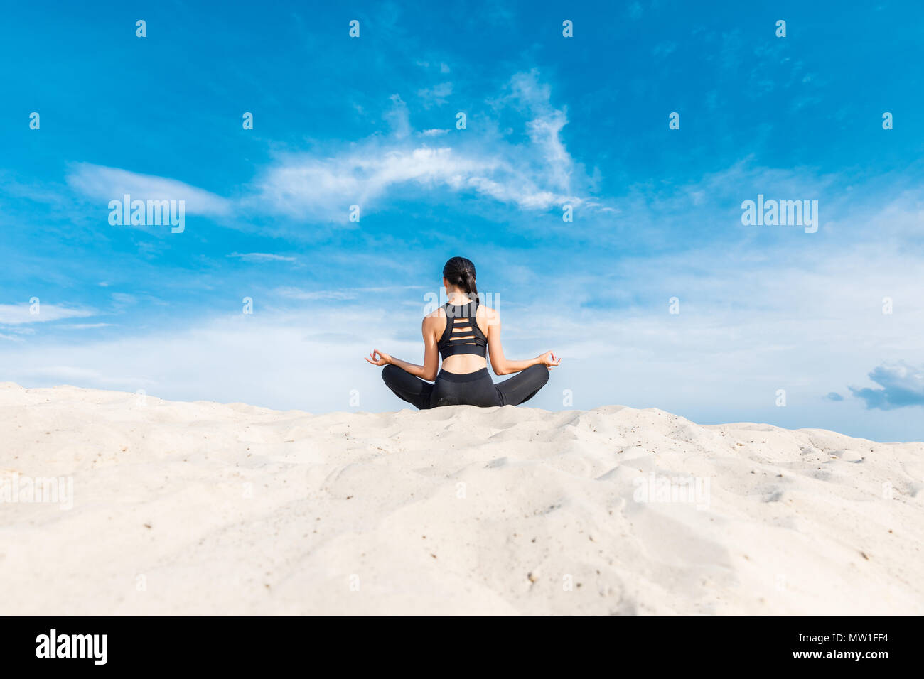 Vista posteriore della donna meditando in lotus yoga pone con gyan mudra sulla sabbia contro il cielo nuvoloso Foto Stock