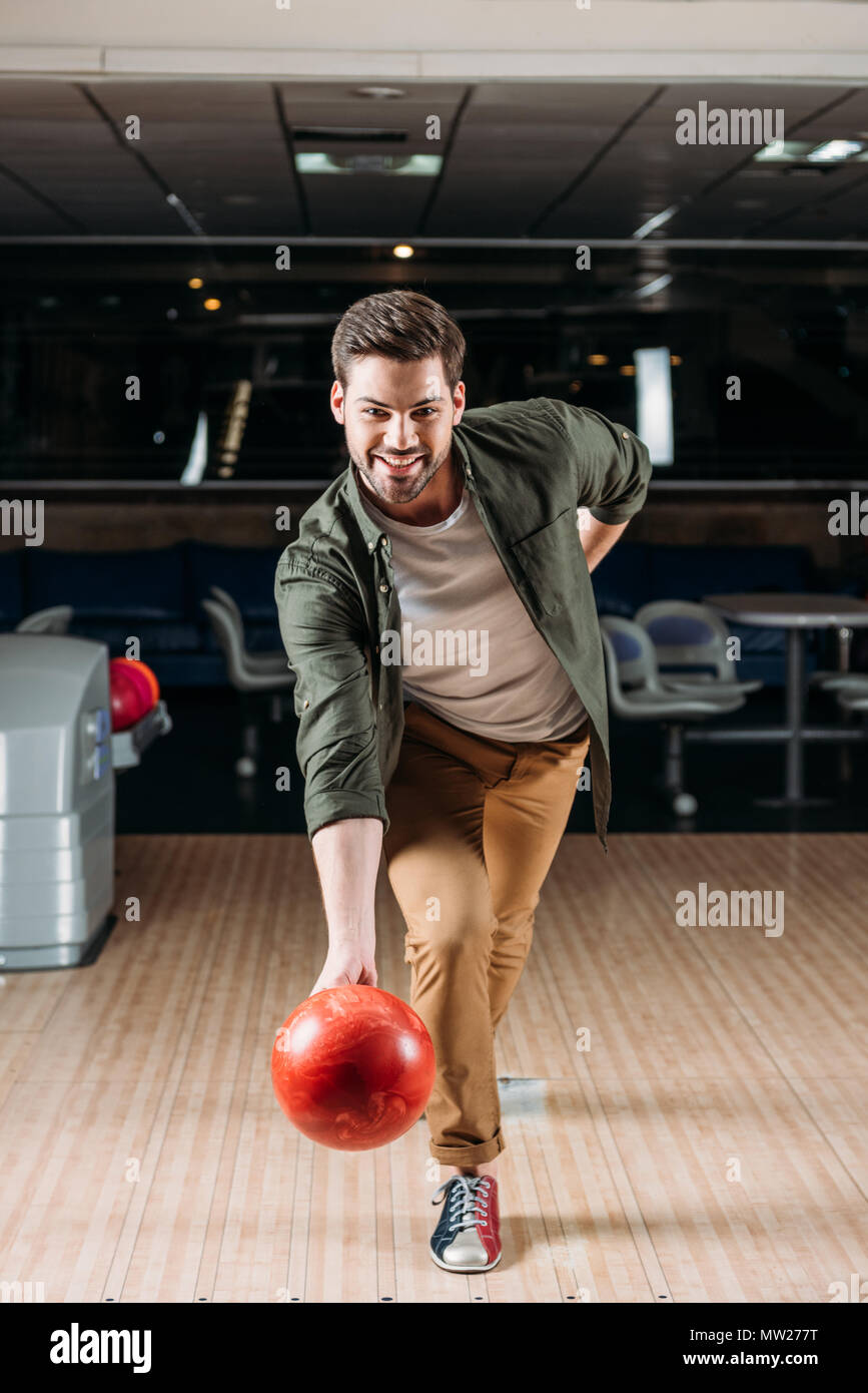 Felice giovane uomo gettando palla da bowling al club Foto Stock