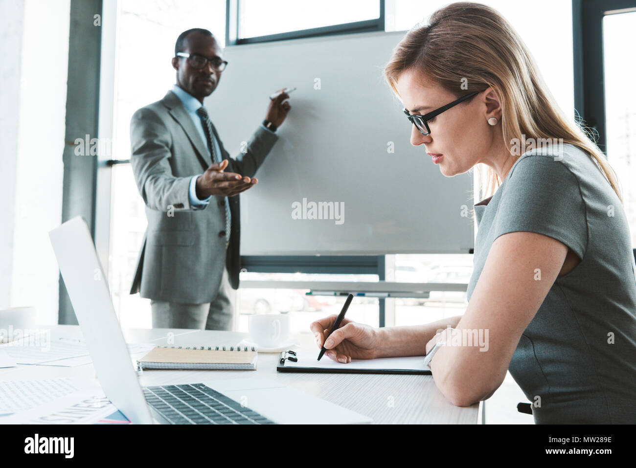 African American businessman puntando alla lavagna e guardando il collega di prendere appunti durante la riunione Foto Stock