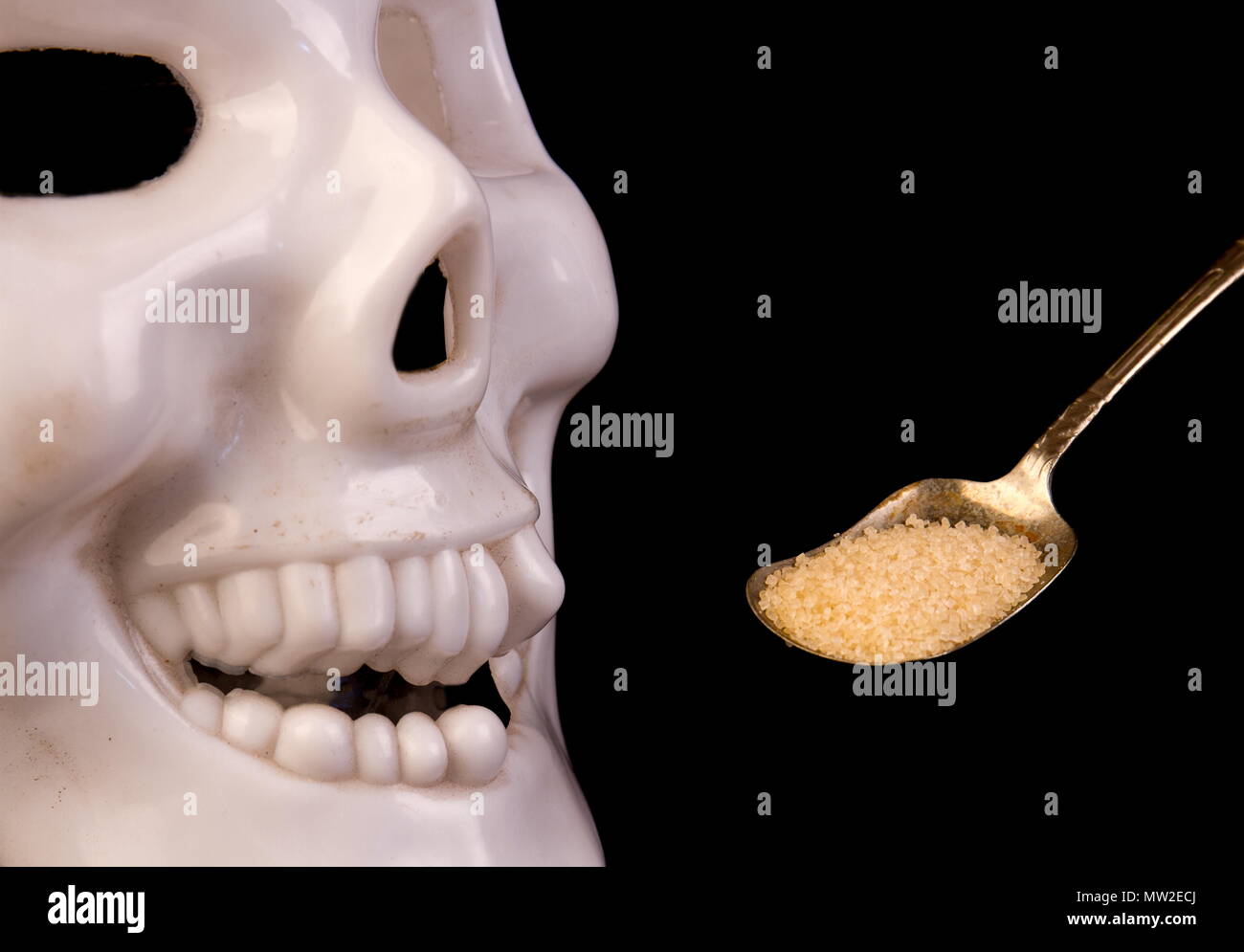 Cranio e un cucchiaio colmo di zucchero - i pericoli di un eccesso di consumo di zucchero - su uno sfondo nero immagine con spazio copia in formato orizzontale Foto Stock