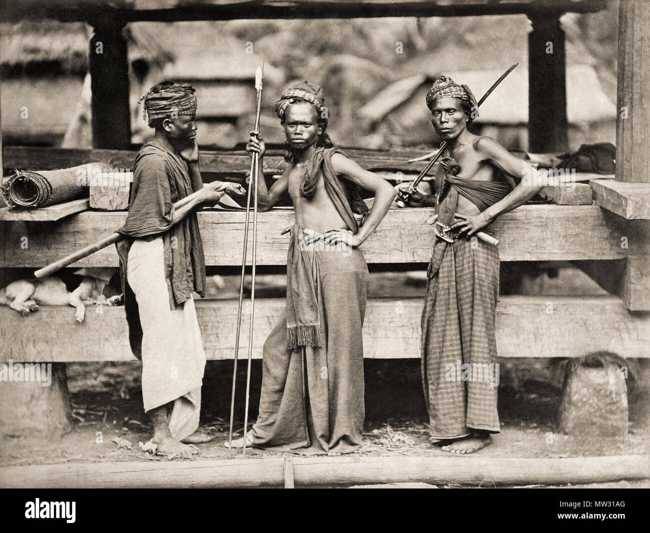 . Portret van een drietal gewapende Batak mannen . Inglese: Tre Batak guerrieri con lance e spade di fronte ad una costruzione in legno. Un cane si trova tra le due travi a sinistra. Deutsch: Drei Batak Krieger bewaffnet mit Speeren und Schwertern stehen vor einer Holzkonstruktion. Zwischen den Balken auf der Linken liegt ein Hund. Nederlands: Drie Karo Batak krijgers bewapend incontrato speren en krissen staan voor een houten constructie. Tussen de balken ligt een hond te slapen. . Circa nel 1870 663 guerrieri Batak 60011135 modifica Foto Stock