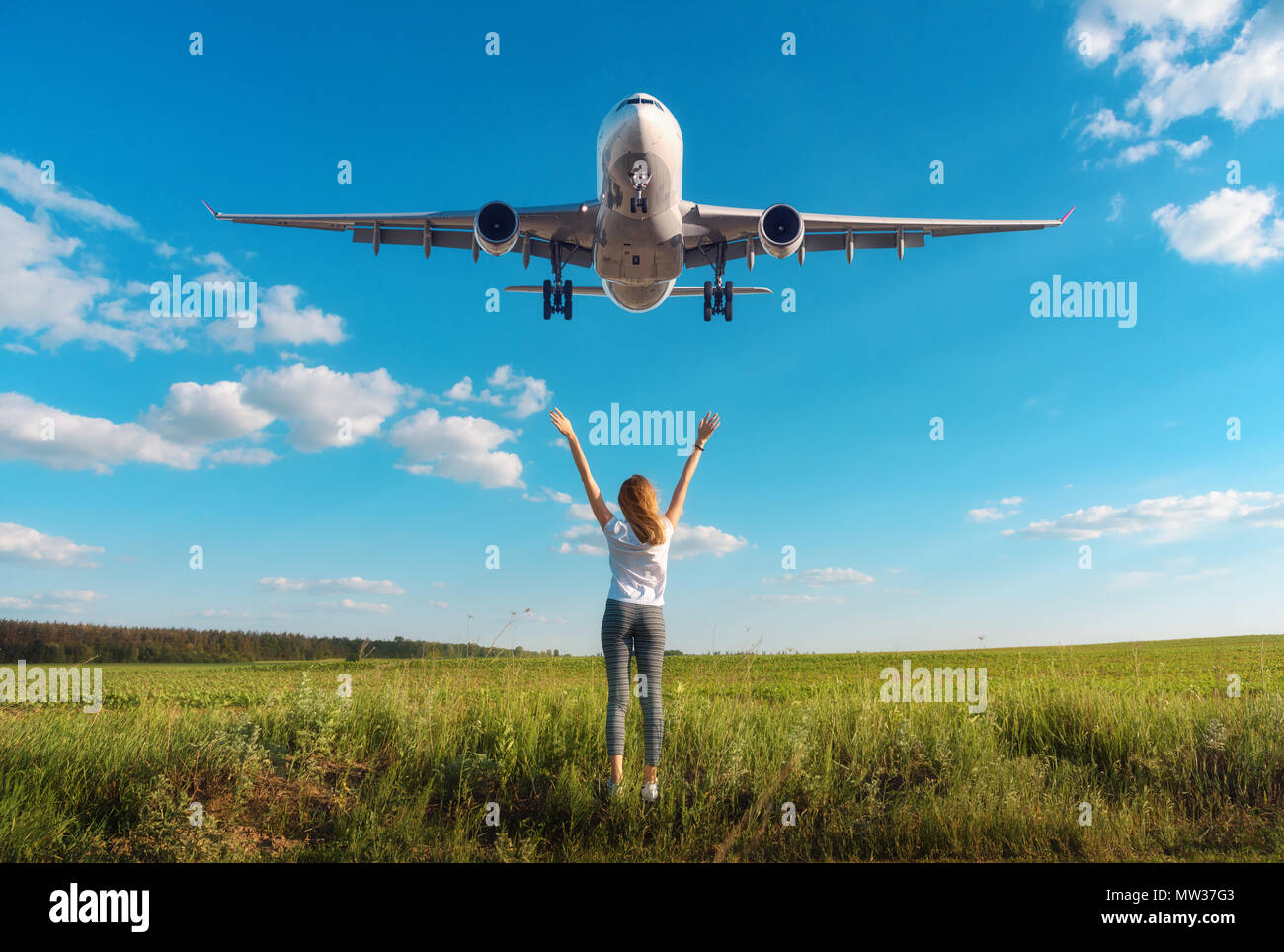Aeroplano e la donna al tramonto. Paesaggio estivo con la ragazza in piedi sul campo in erba sollevata con le armi e Battenti aereo passeggeri nel cielo blu. Wo Foto Stock