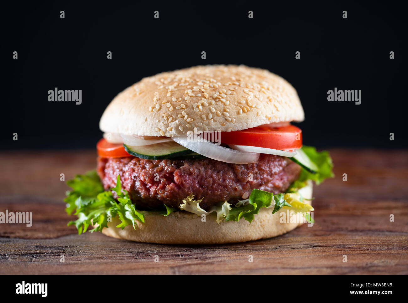 Hamburger in legno scuro con sfondo scuro. Mezzo raro con lattuga, cipolla e pomodoro. Foto Stock