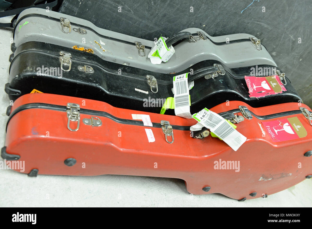 Selezione di diverso colore volo chitarra casi che giace dietro le quinte ad un concerto con carta di imbarco di etichette su di essi Foto Stock