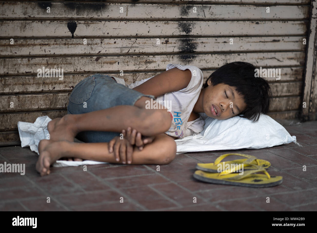 Un bambino che dorme ruvida sul marciapiede nel centro di Cebu City, Filippine Foto Stock