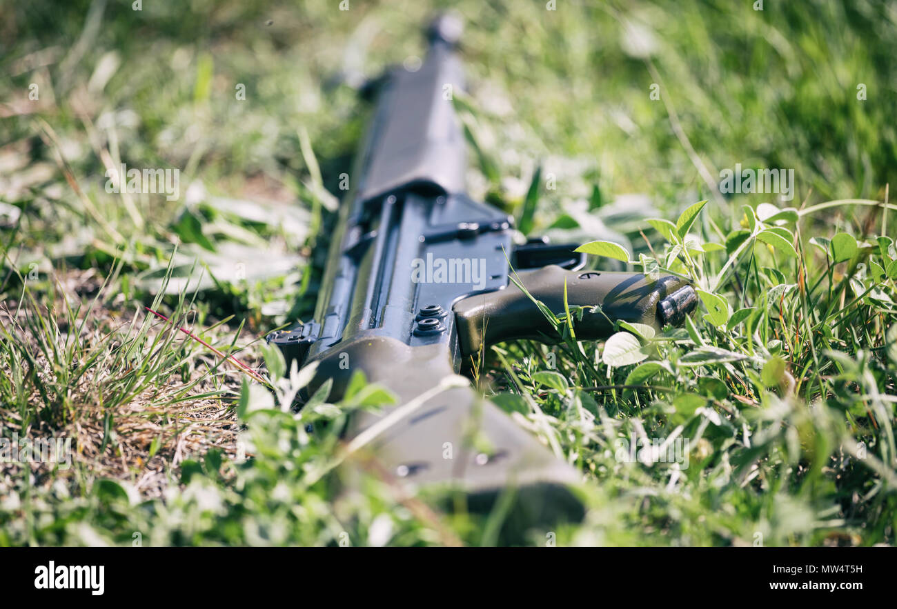 Anti-Nozione di guerra. Pistola arma da fuoco stabilisce su verde erba soldato perché negare ad uccidere. Vista ravvicinata dell'arma sulla natura sfocata sullo sfondo. Foto Stock