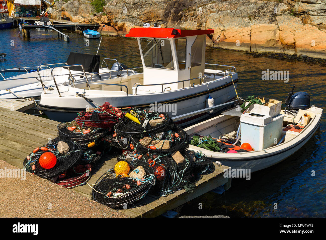 Trappole di pesci e le reti su un molo pronto per l'uso. Barche da pesca ormeggiate presso il molo. Ronnang sull'isola Tjorn, Svezia. Foto Stock