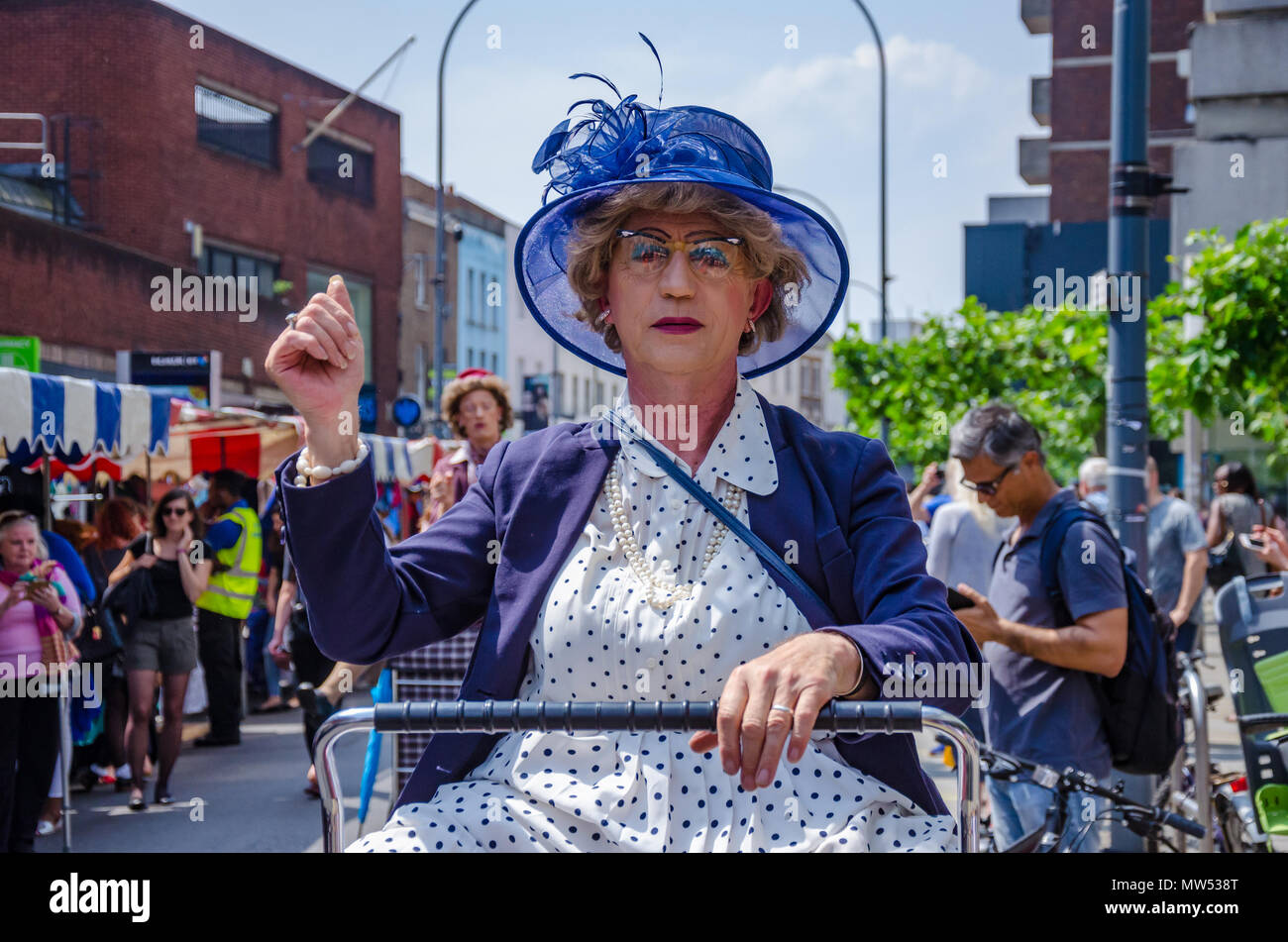 Un uomo vestito come una vecchia donna a cavallo di un carrello della spesa è in realtà un attore di strada divertente la folla a Hammersmith & Fulham Mercato a molla Foto Stock