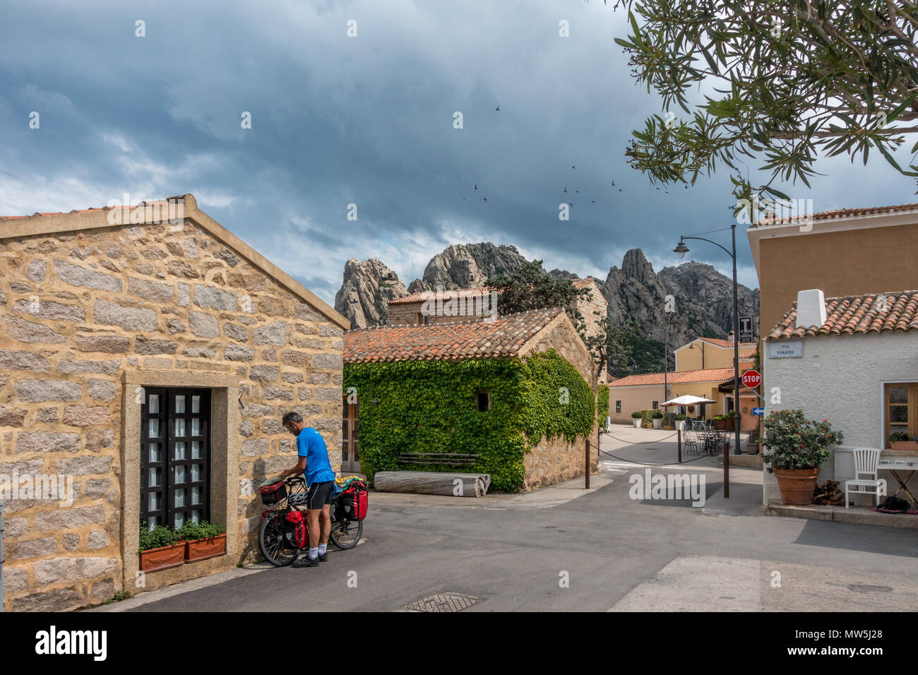 Ciclista con bici da turismo e canestri di fermarsi per una sosta nel bellissimo borgo di San Pantaleo con rondoni nel cielo, Sardegna, Italia Foto Stock