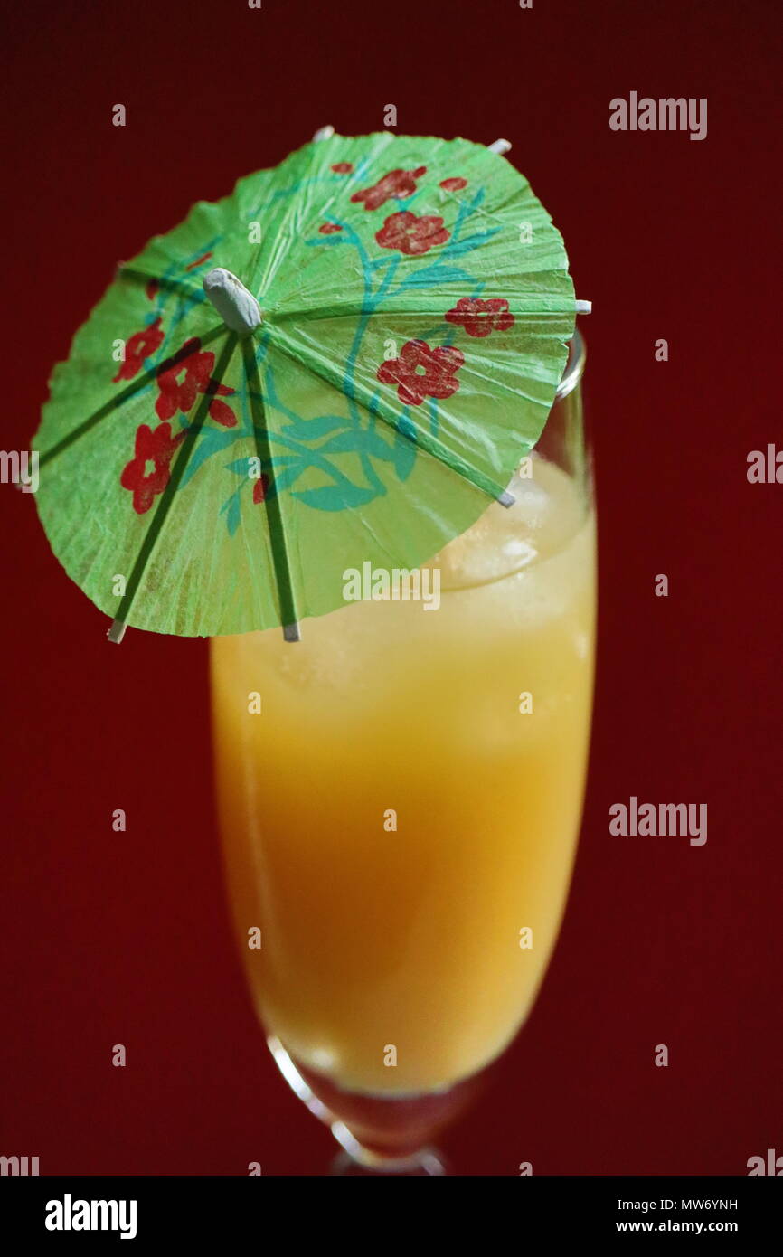 Deliziosi succhi di arancia drink sul ghiaccio con ombrello contro lo sfondo rosso Foto Stock