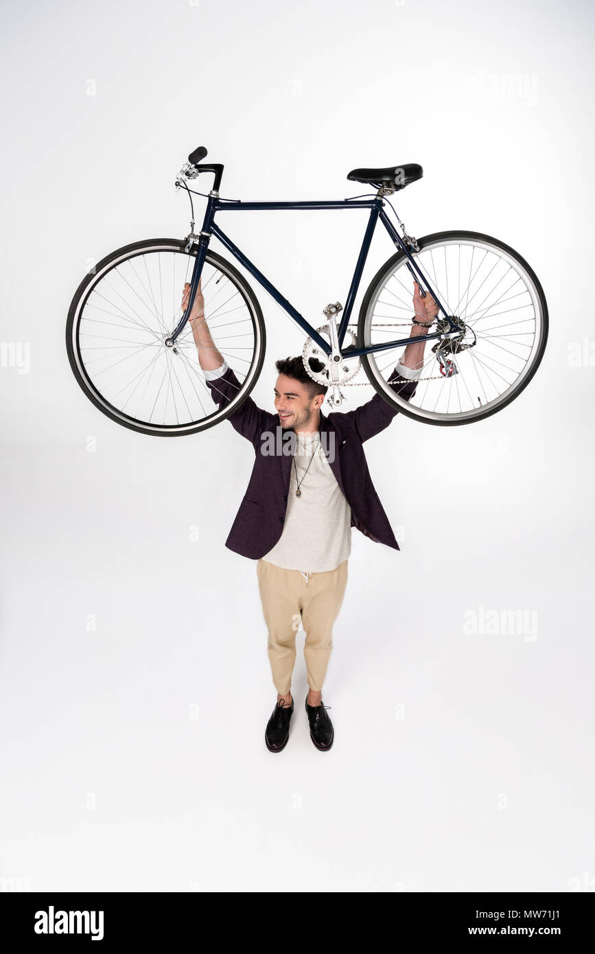 Angolo di alta vista sorridente giovane azienda bicicletta sopra la testa e lo sguardo lontano Foto Stock