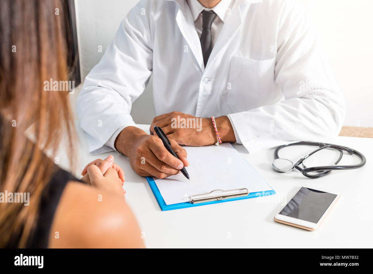 Il medico e il paziente stanno discutendo circa la diagnosi. Medico tenendo uno stetoscopio e prendere appunti. Foto Stock