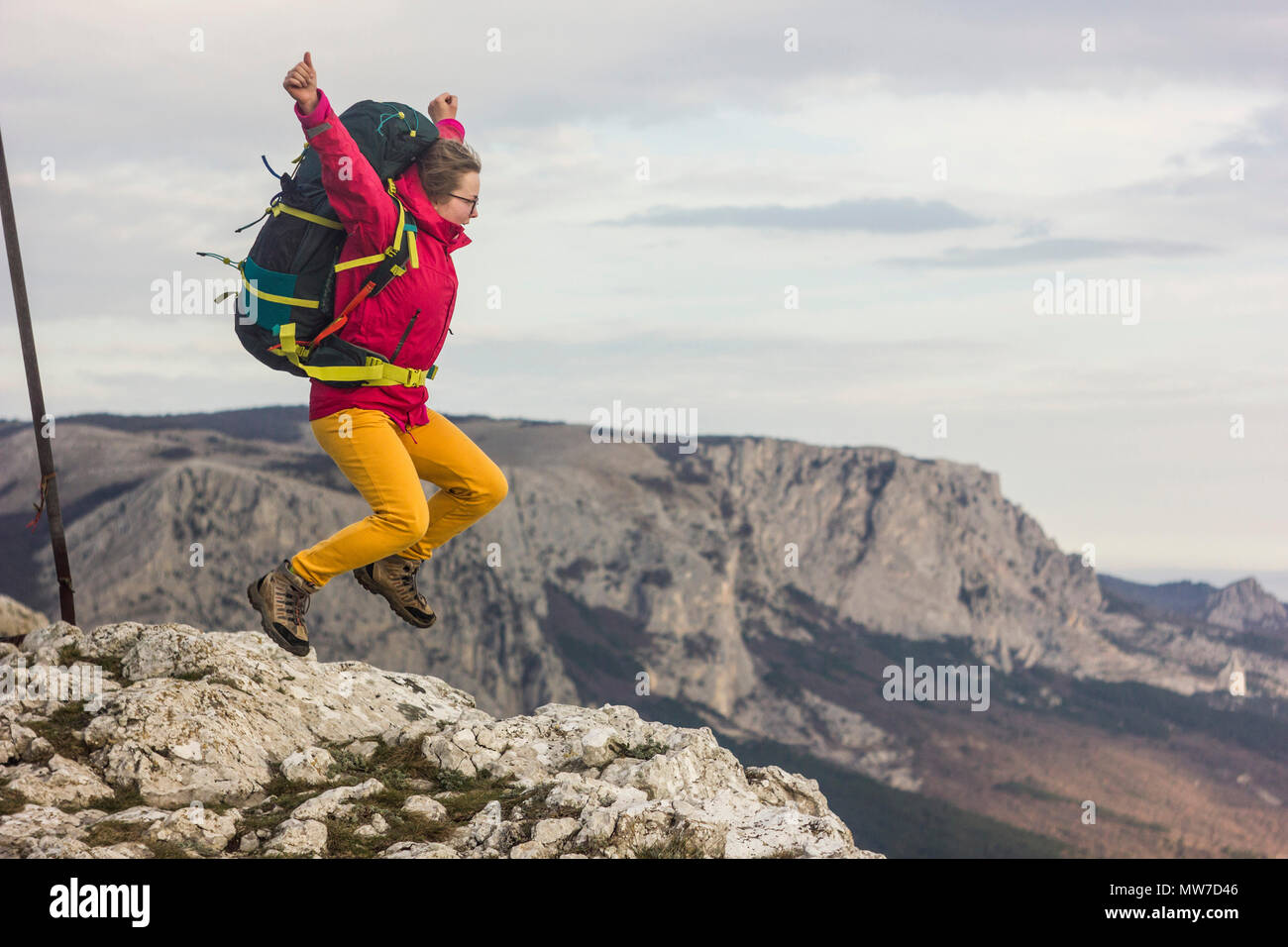Ragazza con zaino saltando su una scogliera in montagna Foto Stock