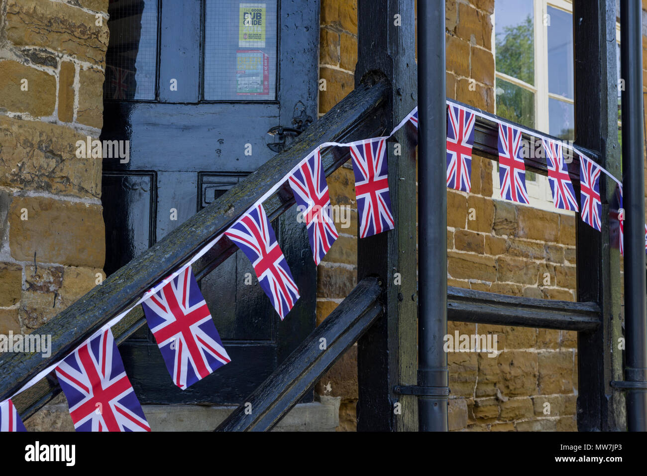 Una fila di piccoli Union Jack infilate le bandiere lungo un corrimano in legno al di fuori di un village pub; grande Brington, Northamptonshire, Regno Unito Foto Stock