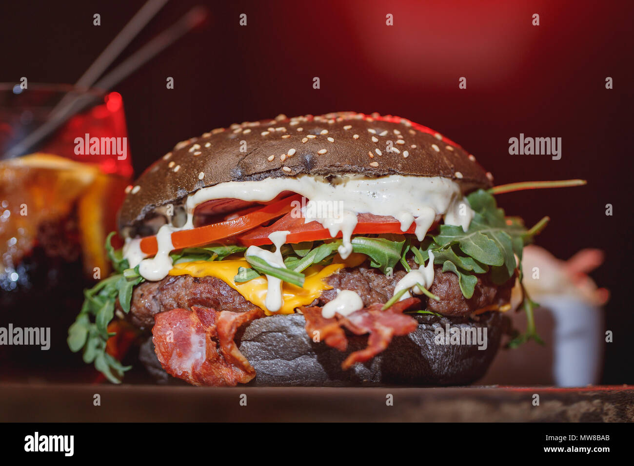 Fresh Hamburger classico con carne, formaggio, pancetta, cipolla, pomodoro e rucola su un tavolo di legno. Foto Stock