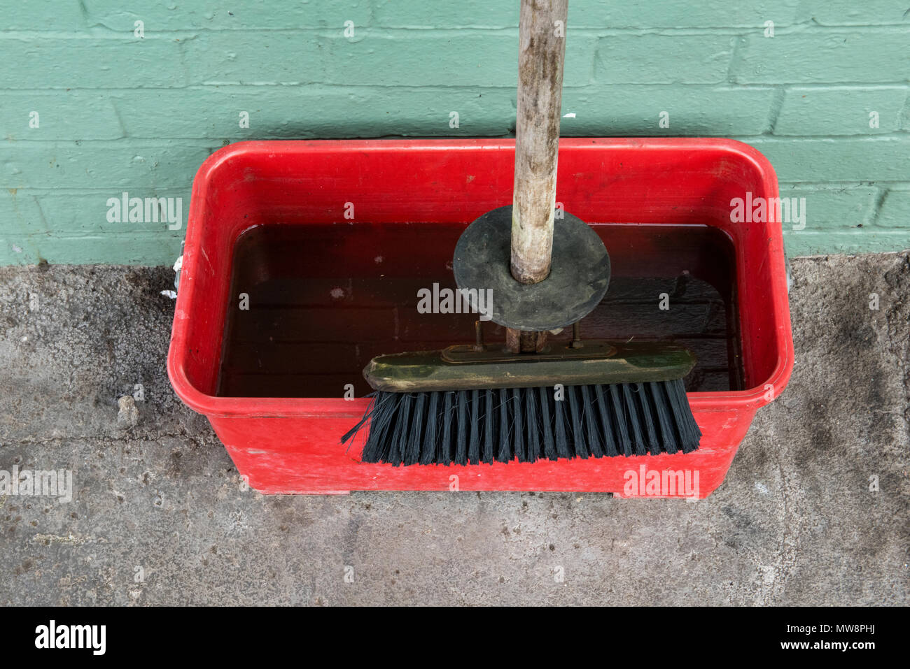 Un mop o pennello e secchio pieno di acqua sporca appoggiata contro un muro dopo che è stata utilizzata per la pulizia. Impugnatura in legno spazzola e acqua sporca. Foto Stock