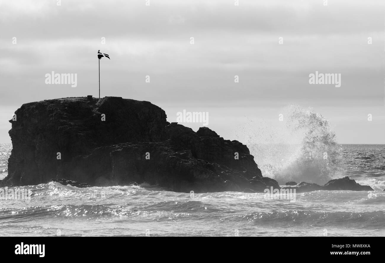 Perranporth Cappella, rock Cornish bandiera di St Pirran, volare sulla roccia, con un'onda di schiantarsi contro la roccia creando una curva di acqua bianca Foto Stock