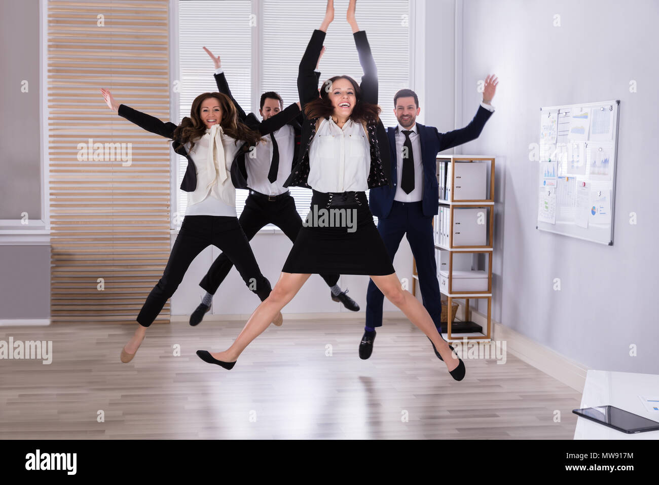 Giovani Imprenditori Jumping in Office alzando le braccia Foto Stock
