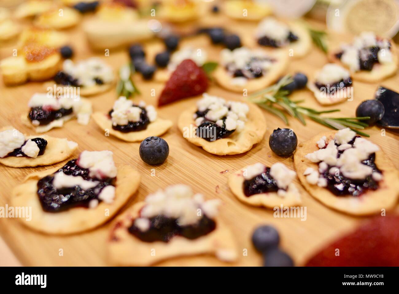 Delizioso e stuzzicante il formaggio Feta con ribes cracker sul display sul tagliere di legno con rosmarino, mirtilli e fragole USA Foto Stock