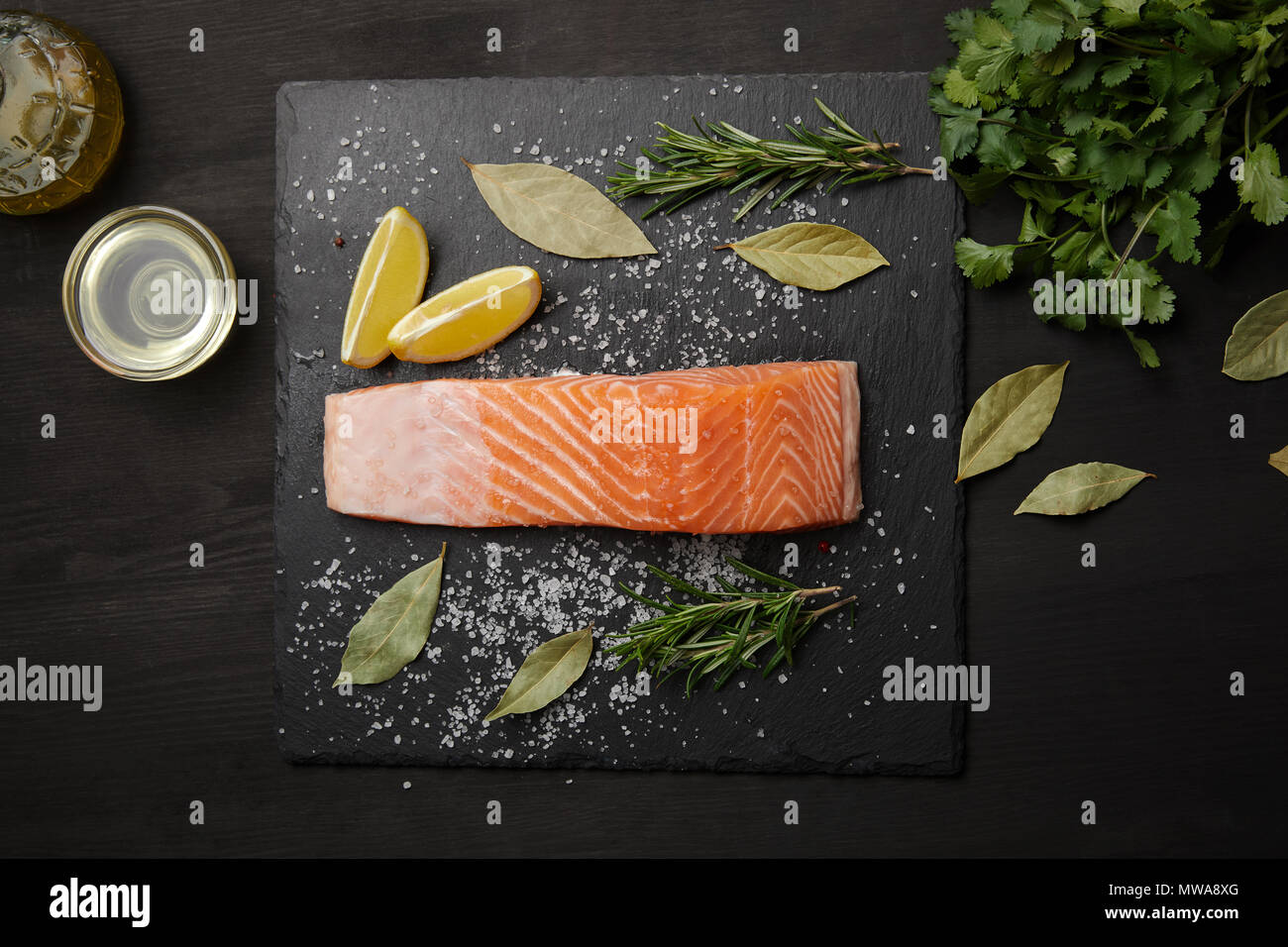 Pezzo di salmone con sale sulla tavola nera con limone e erbe aromatiche Foto Stock