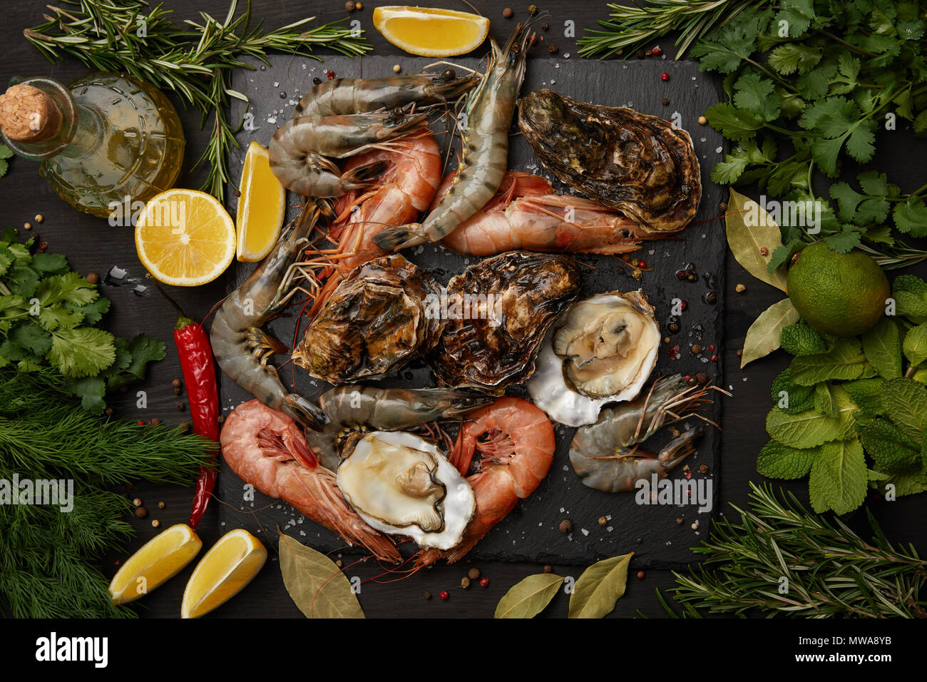 Gamberetti e ostriche sulla scheda di ardesia con erbe e limoni Foto Stock