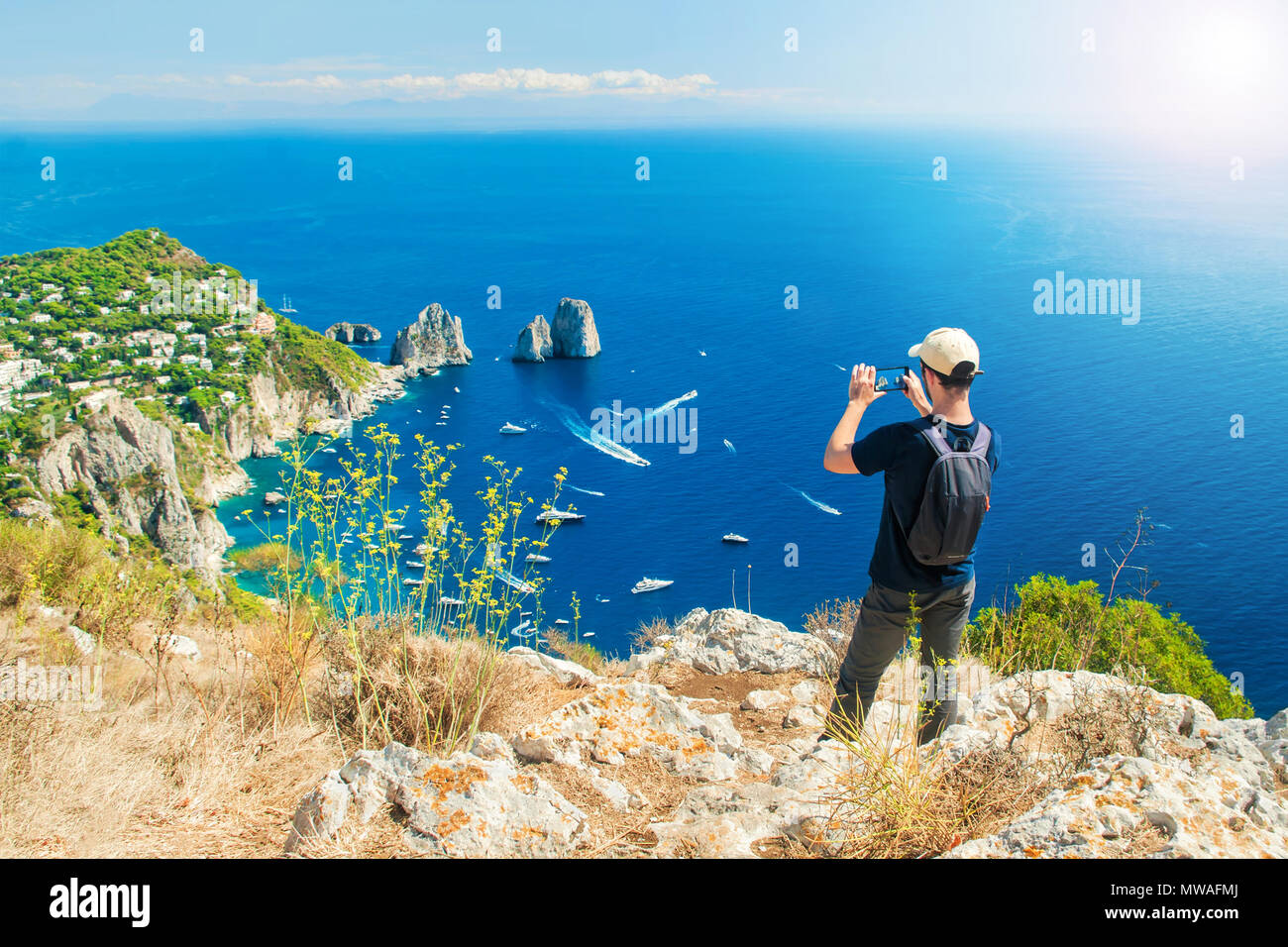 Giovani caucasici turistica prendendo foto di famosi faraglioni in mare con il suo smartphone sulla sommità del Monte Solaro dopo escursioni fino il sentiero di Capri Foto Stock