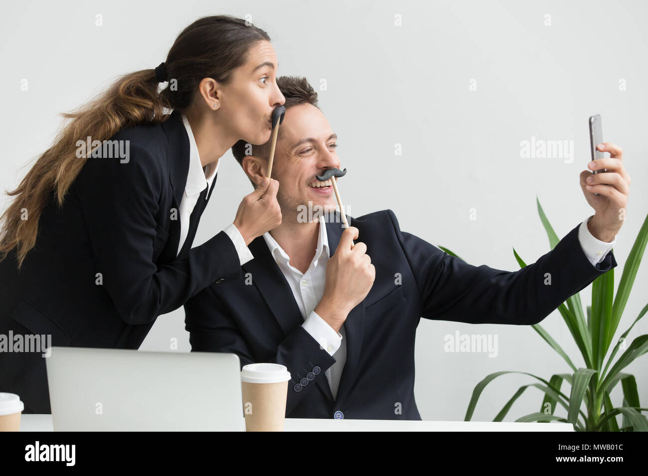 Gentili colleghi smorfie holding baffi finti tenendo selfi Foto Stock