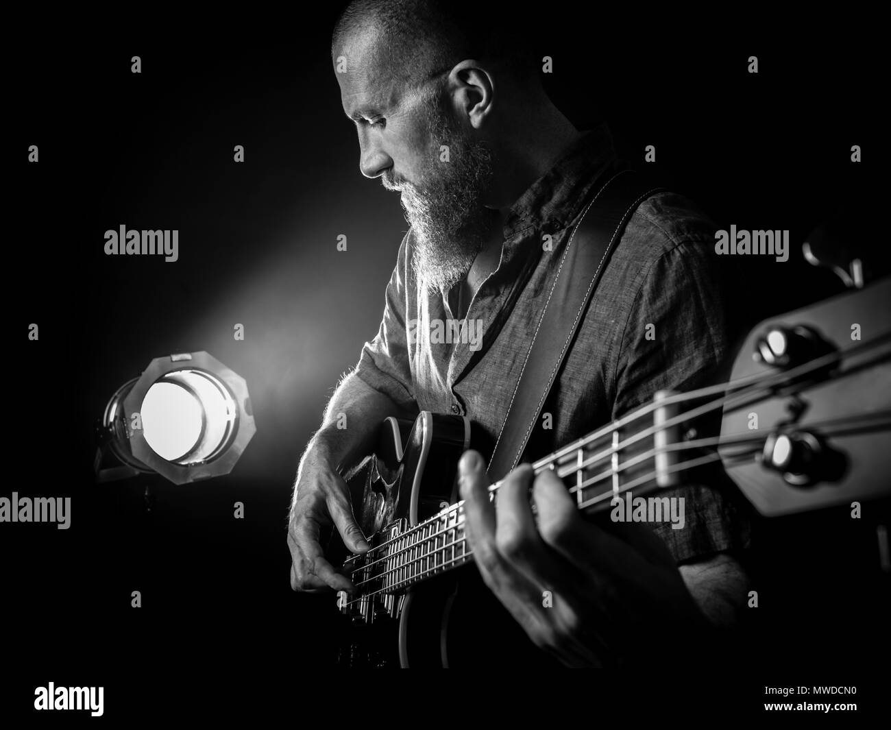 Foto di un uomo barbuto suonare chitarra basso sul palco di fronte a faretti. Foto Stock