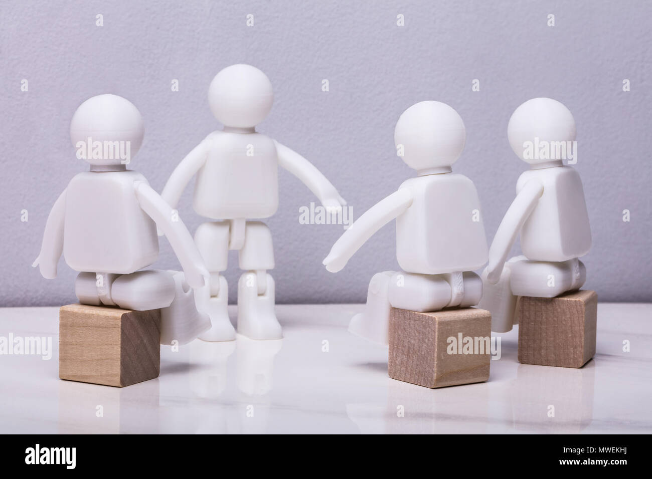 Bianco una figura umana in piedi di fronte ad altre tre cifre bianche seduta il blocchetto in legno Foto Stock