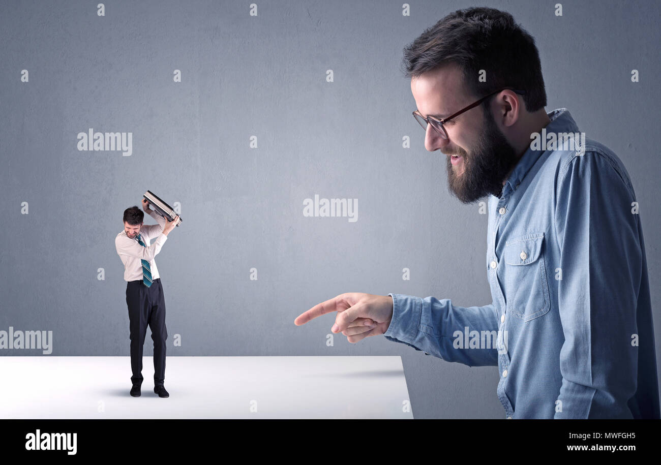 Giovane imprenditore professionale essendo arrabbiato con un altro imprenditore in miniatura nella parte anteriore di un bluastro sfondo grigio Foto Stock